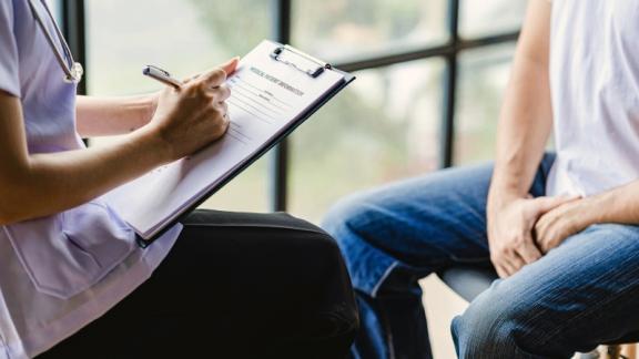 Doctor taking notes from a patient by a window.