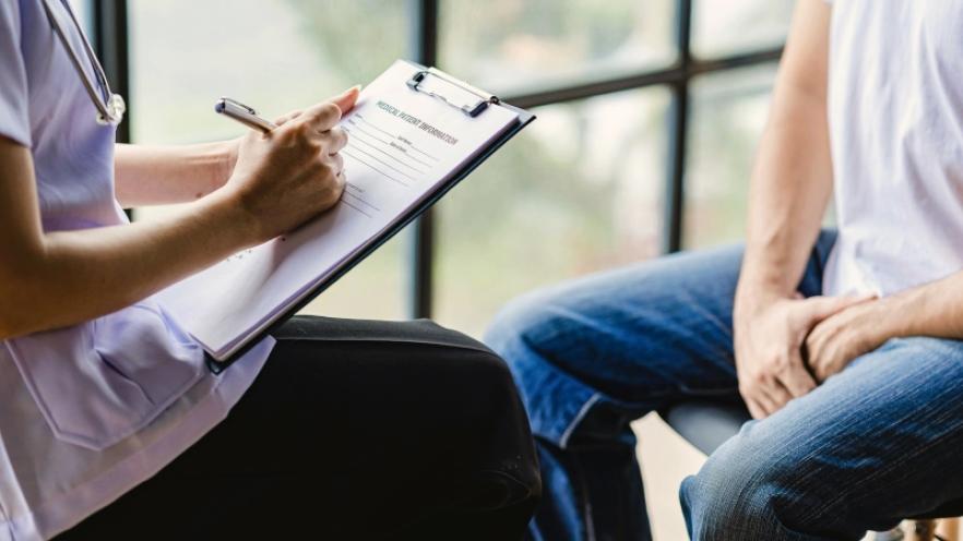 Doctor taking notes from a patient by a window.