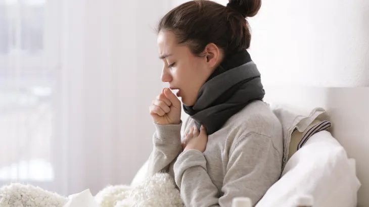 Image of a women in bed coughing